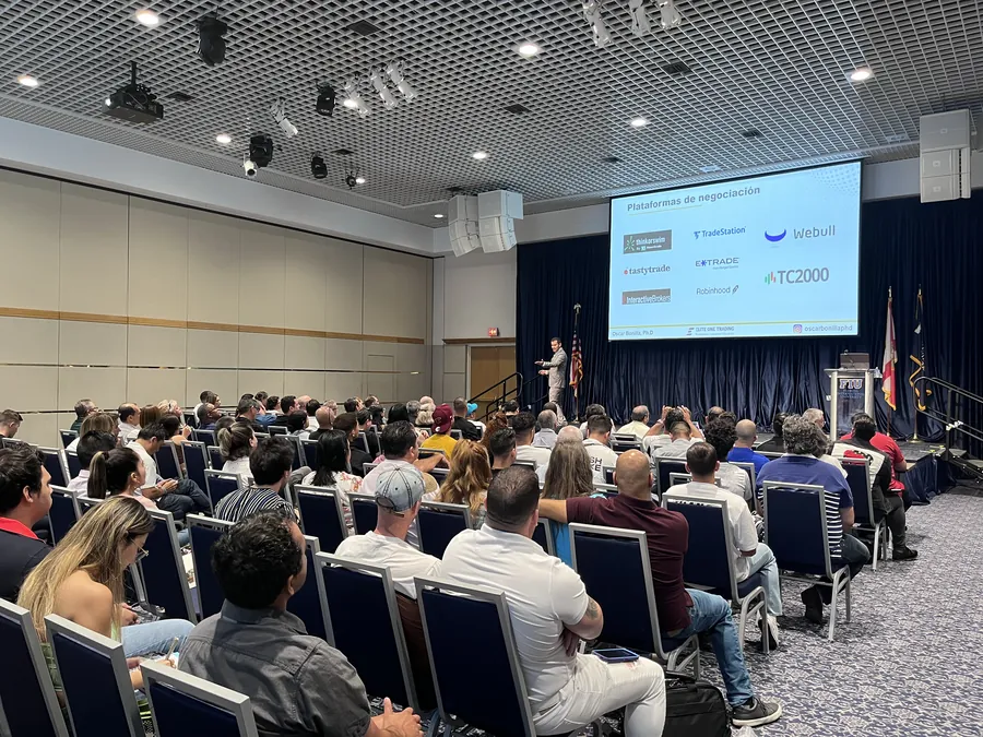 Asistentes en un evento presencial, con las plataformas de trading proyectadas